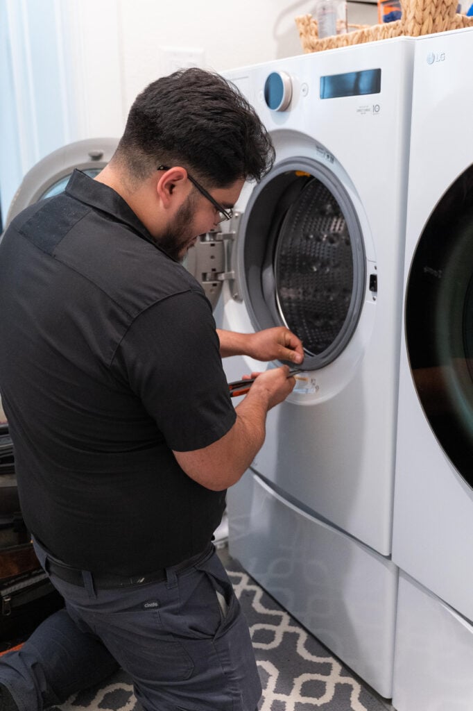 Technician repairing a front-loading washing machine in a laundry room