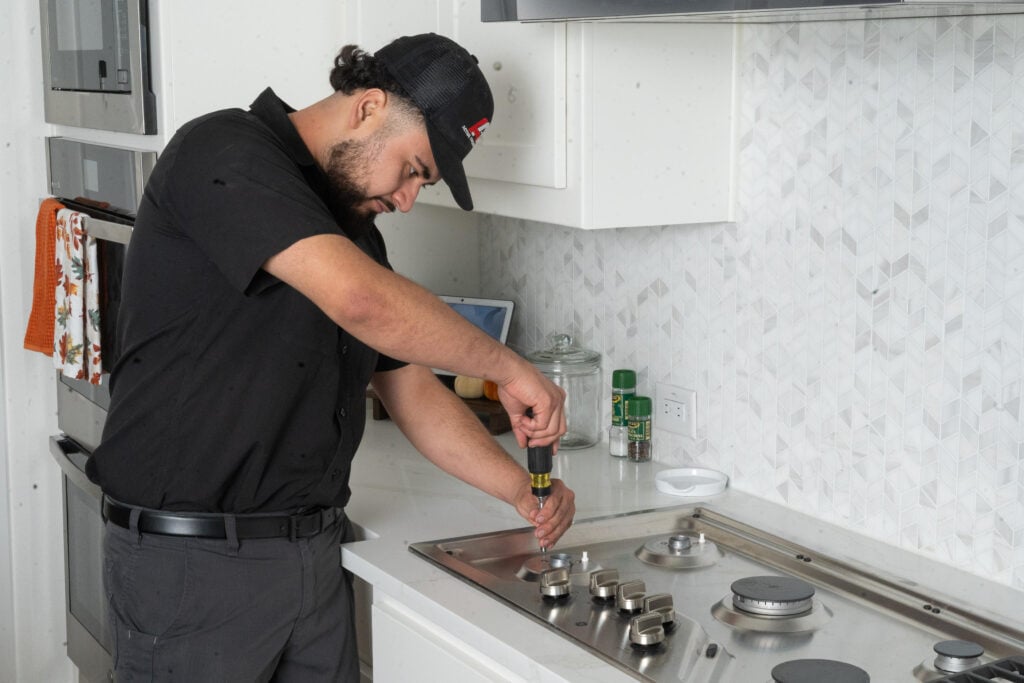 Technician using a screwdriver to install a kitchen gas stove in a modern kitchen
