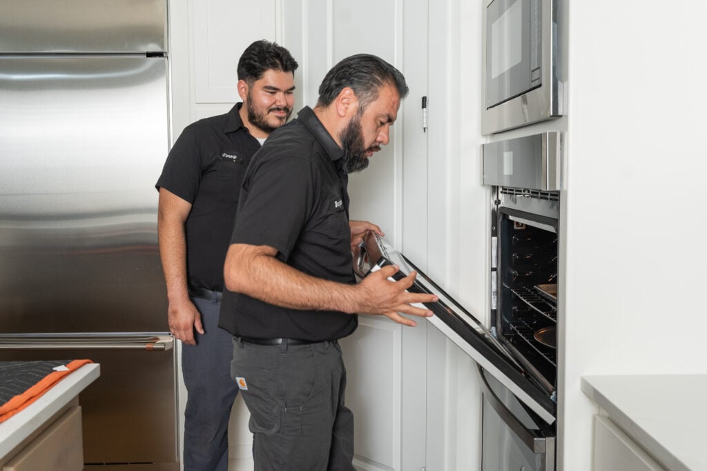 Technician opening a wall oven door while a teammate looks on