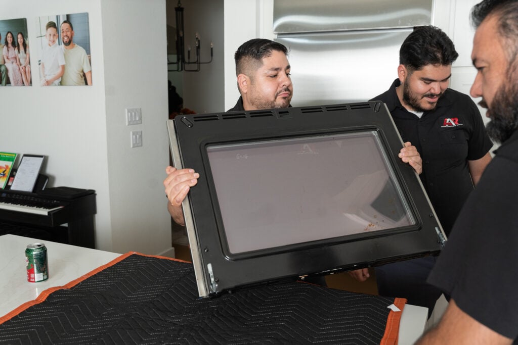 Action Appliance Repair team holding a removed oven door in a customer kitchen