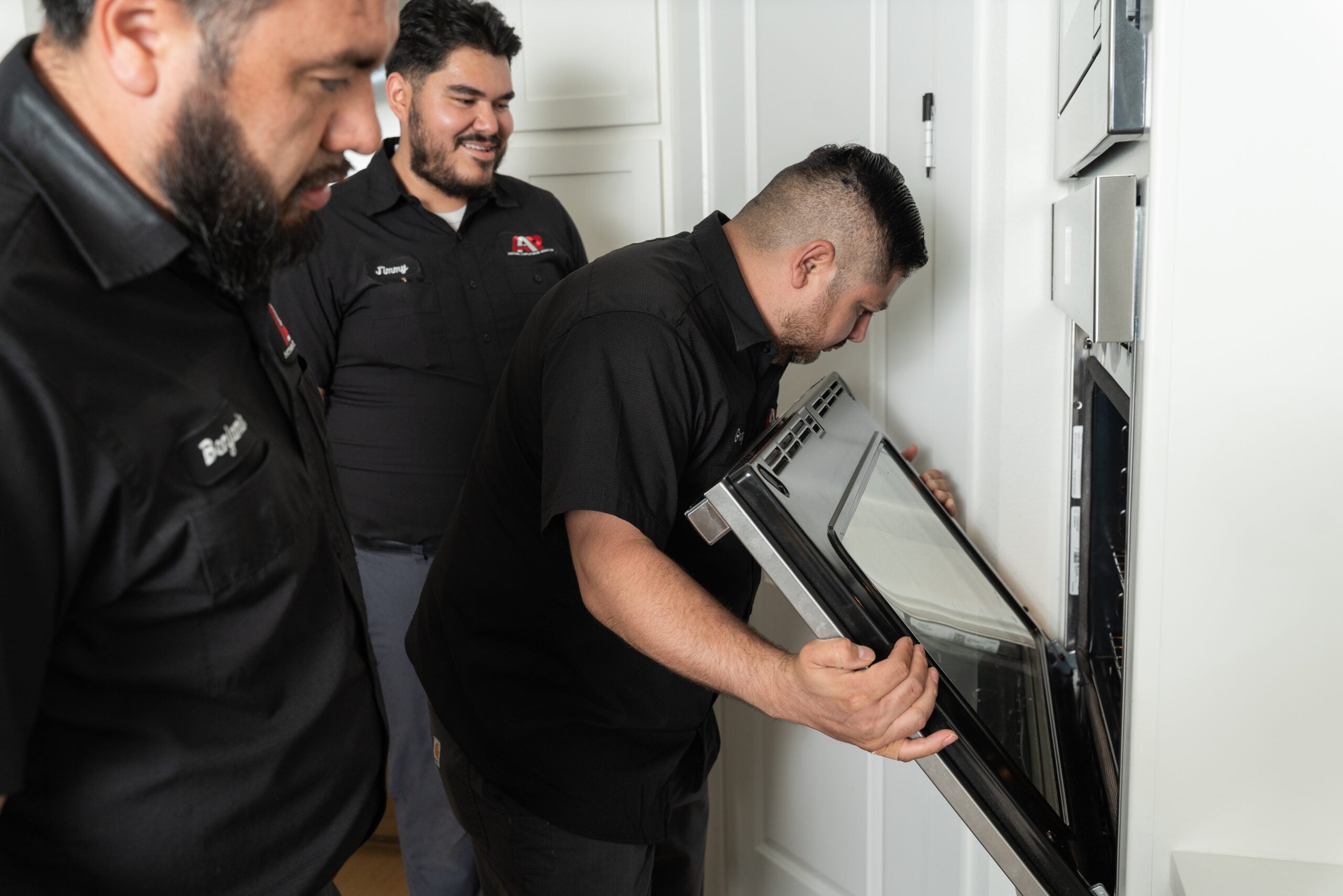 Three Action Appliance Repair technicians inspecting a wall oven