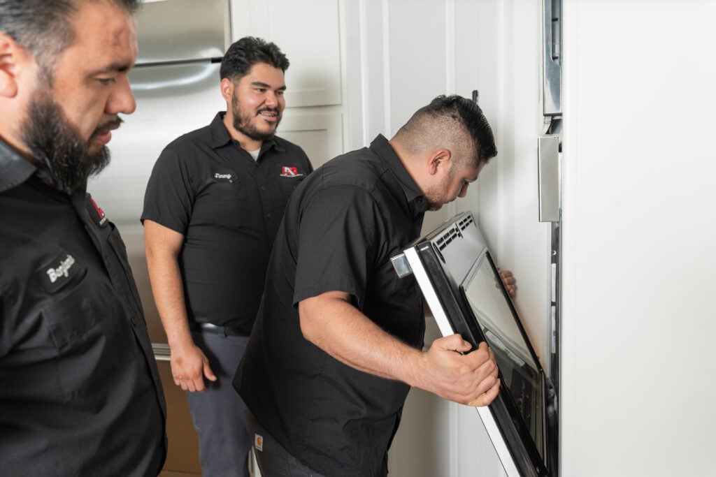 Action Appliance Repair technician opening a wall oven door while two teammates look on