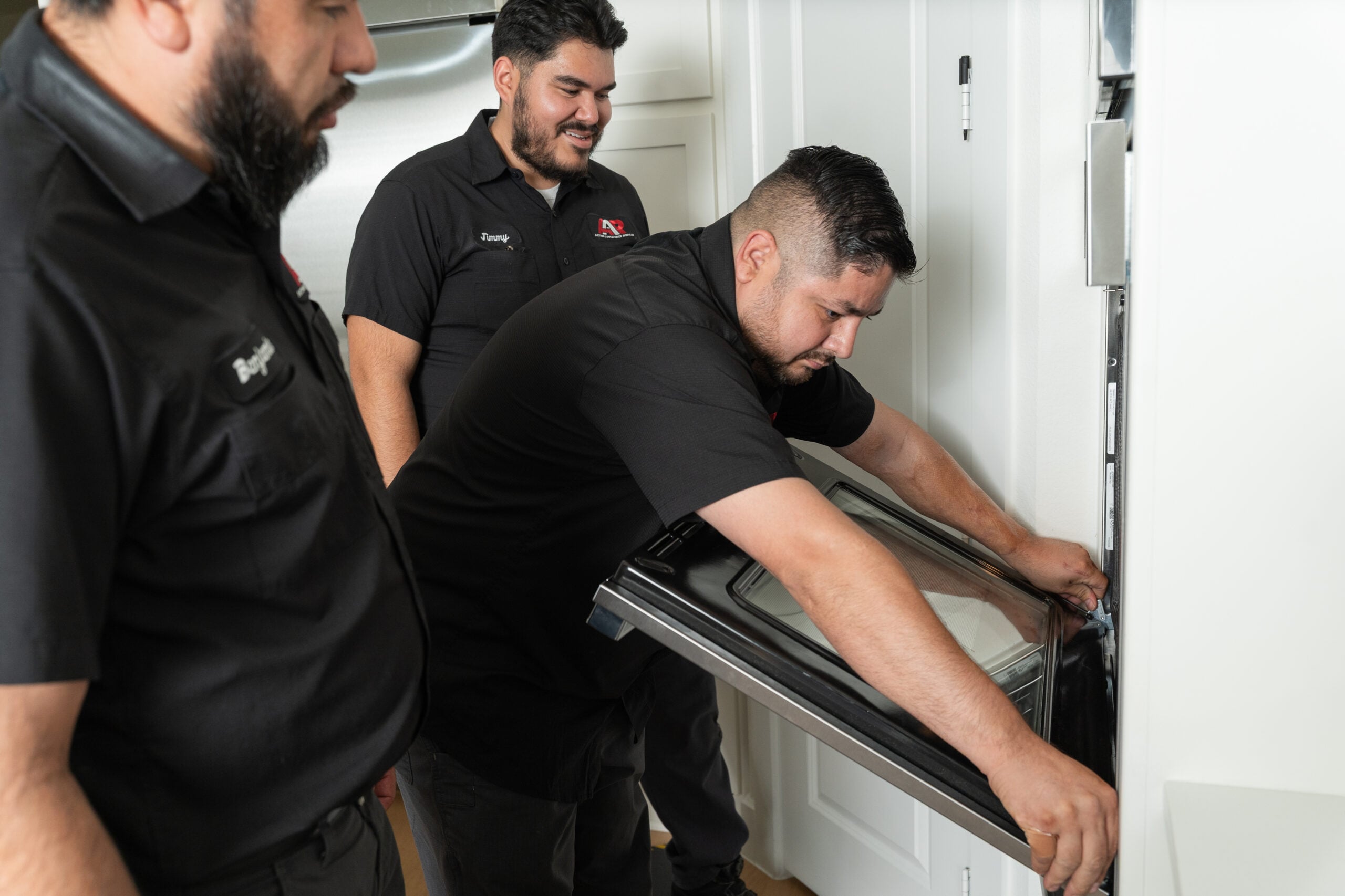 Action Appliance Repair technician pulling open a wall oven door as two teammates watch