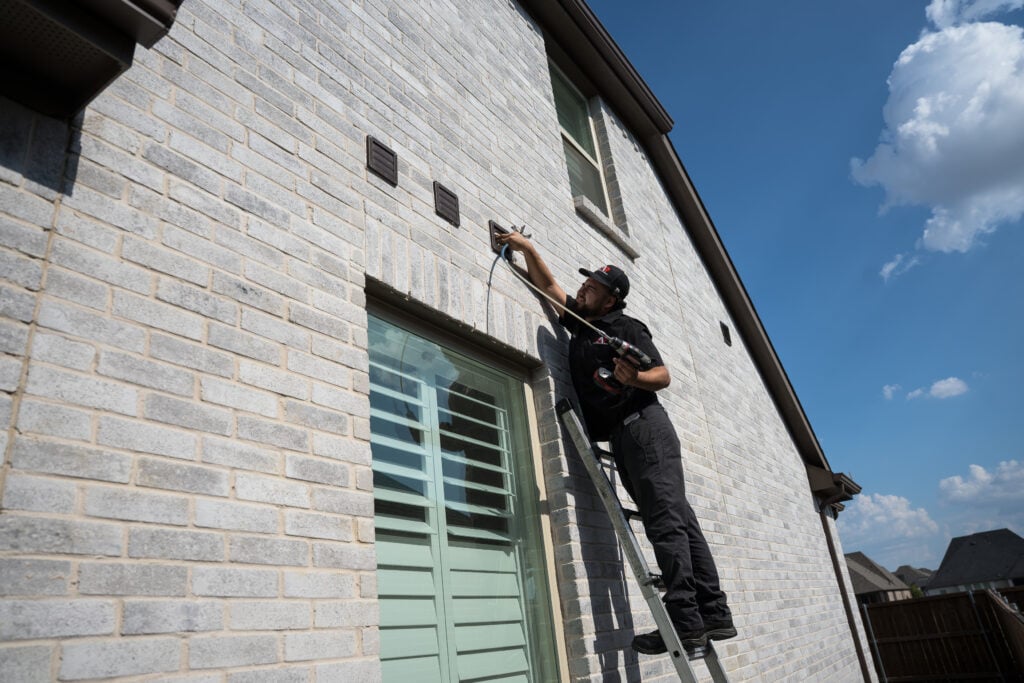 Technician on a ladder cleaning an exterior dryer vent on a brick home