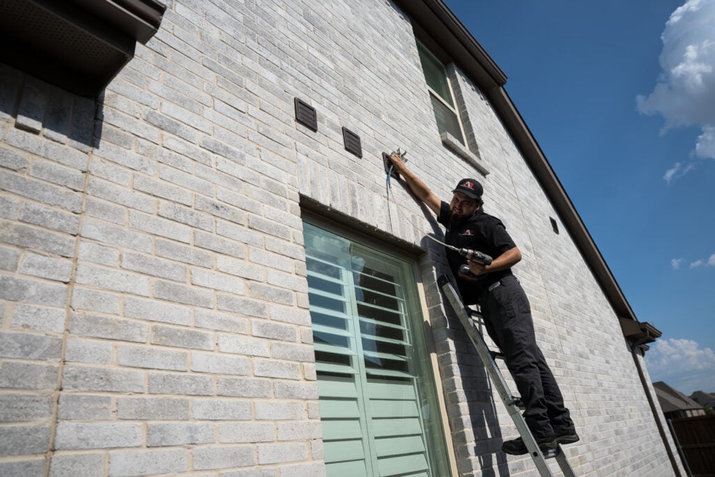 Action Appliance Repair technician on a ladder cleaning a dryer vent on a brick home