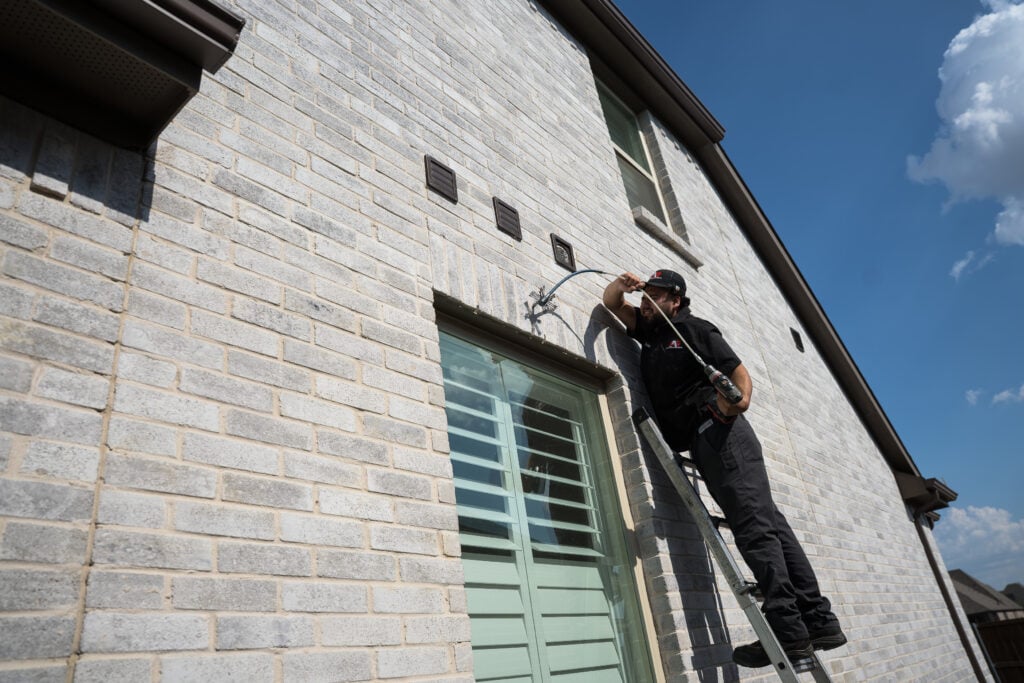 Technician on a ladder servicing a dryer vent outside a home