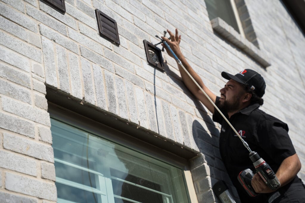 Technician reaching up to clean a dryer vent cover on a brick wall
