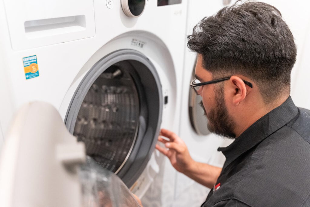 Person examining the interior of a washing machine in a laundry room