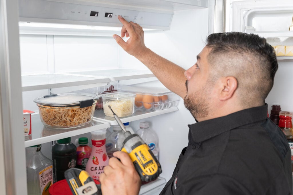 Man using a drill to adjust the temperature setting inside a refrigerator
