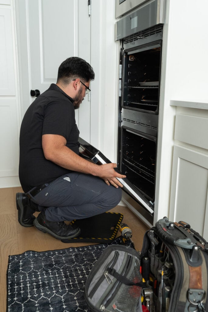Technician inspecting an oven, with tools and a work mat nearby