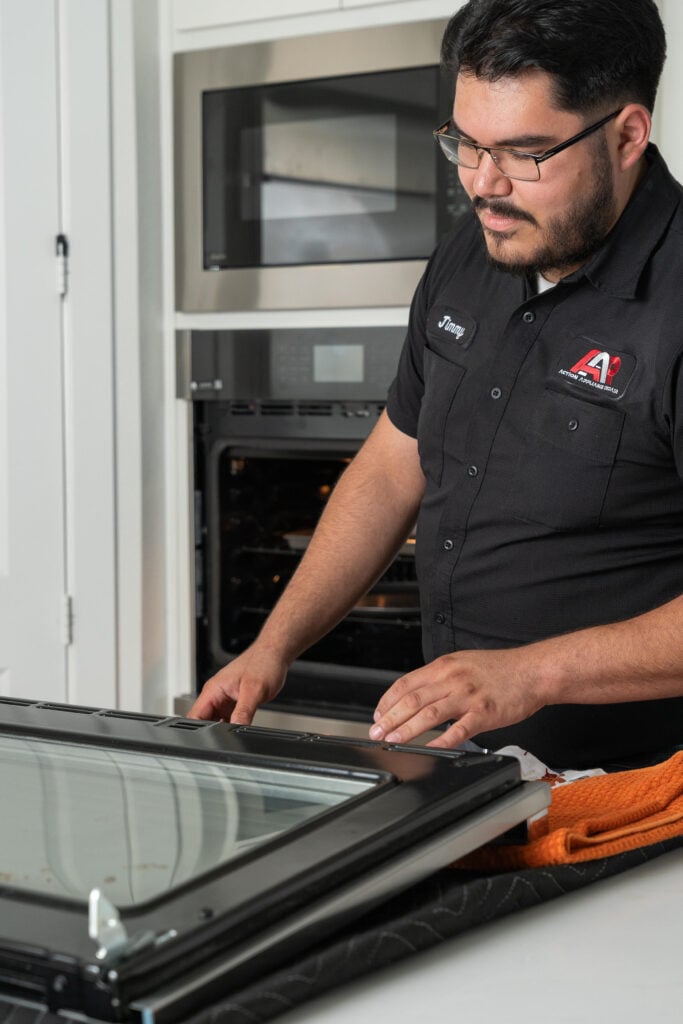 A technician inspecting the glass door of an oven in a kitchen