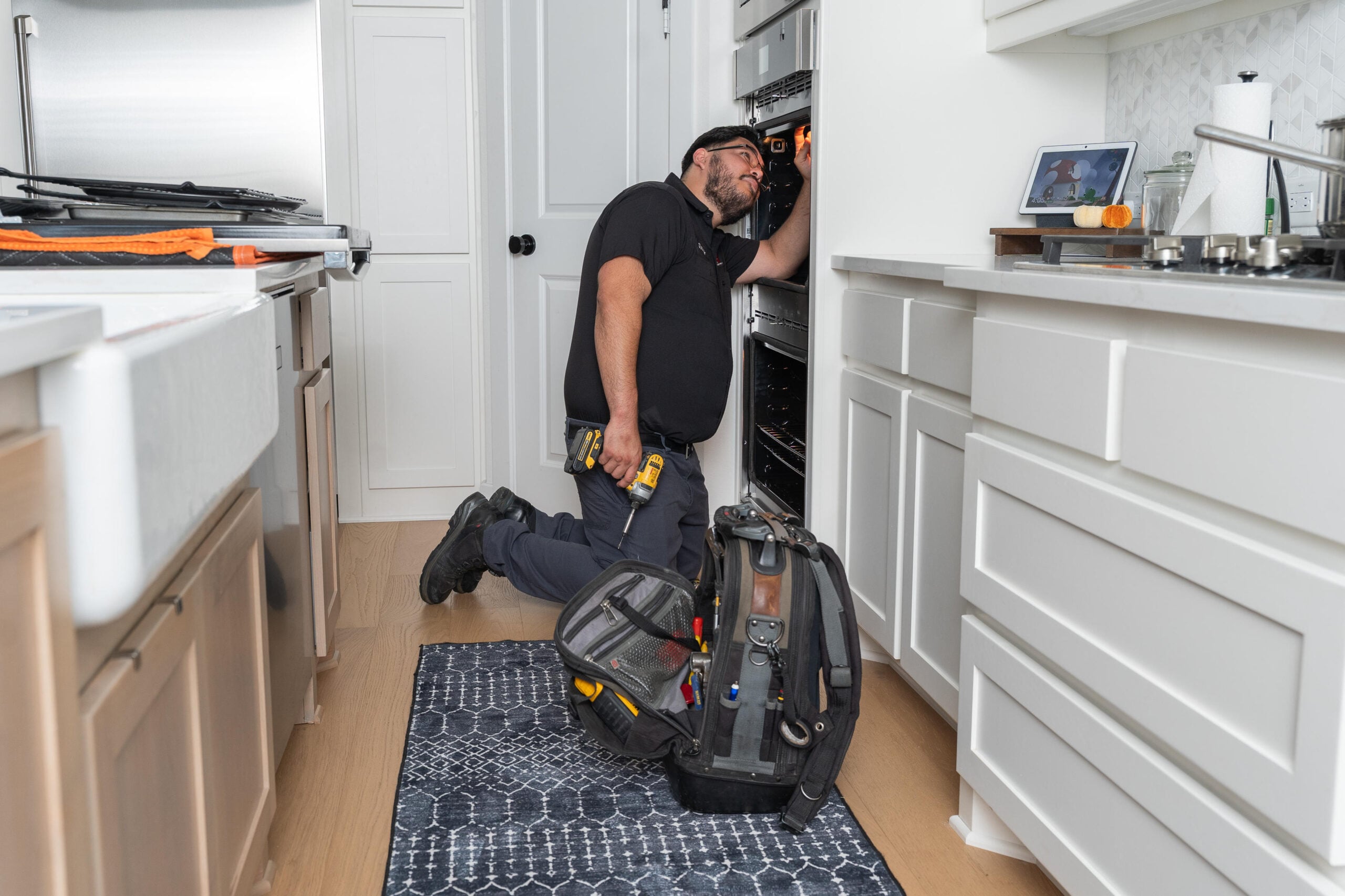 A technician kneeling in a kitchen, examining an oven with a toolkit beside him